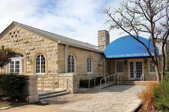 Vista exterior del Hancock Recreation Center con fachada de piedra y marquesina azul