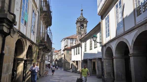 Vista diurna de calle peatonal con edificios coloniales y campanario al fondo