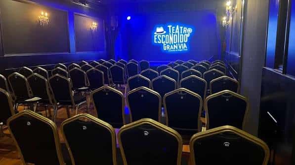 Interior del auditorio con butacas negras y escenario iluminado en azul