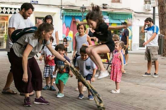 Actividad comunitaria al aire libre con niños jugando a la comba frente a la fachada de La Parcería