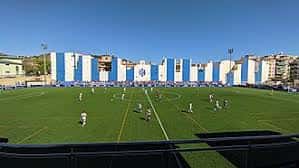 Campo de juego durante un partido con fondo de graderío blanco y azul