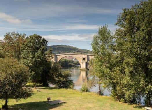 Paisaje natural junto al río con el puente de piedra reflejado en el agua