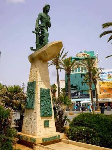 Vista completa del Monumento al Hombre del Mar en Torrevieja con palmeras y edificios de fondo