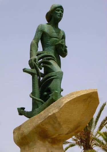 Primer plano de la estatua del hombre del mar sosteniendo un ancla sobre una base rocosa