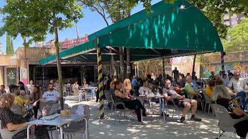 Vista amplia de la terraza con público sentado bajo árboles y toldos verdes