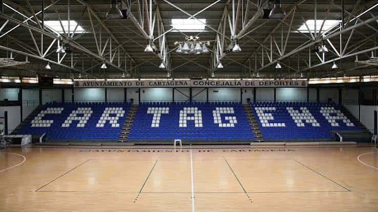 Interior del pabellón con gradas azules y pista de madera para eventos deportivos