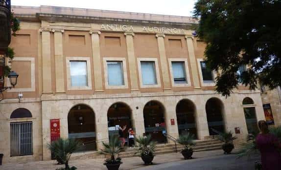Fachada principal del edificio durante el día con personas entrando y plantas decorativas