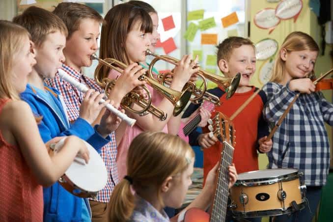 Clase de música con niños tocando instrumentos como trompetas, flauta y guitarra