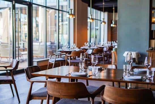 Mesas dispuestas para cena junto a grandes ventanales