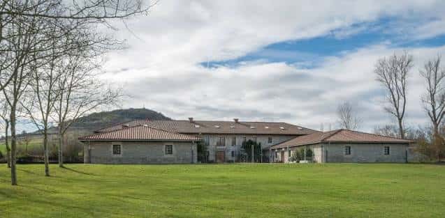 Fachada principal de la Casa de la Dehesa rodeada de prado y árboles
