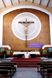 Altar principal de la Parroquia de San Agustín en Linares, con crucifijo central y bancos de madera