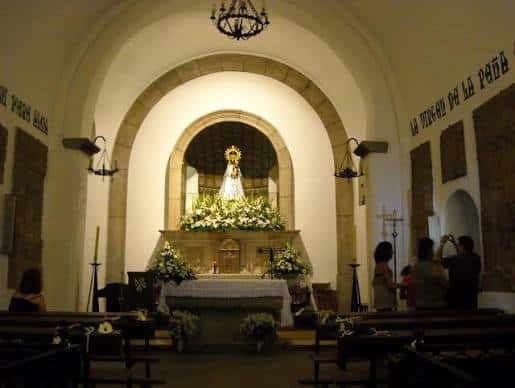Interior del altar principal con la imagen de la Virgen rodeada de flores y visitantes orando