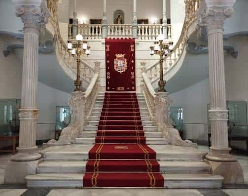 Escalera interior monumental con alfombra roja y detalles ornamentales en mármol