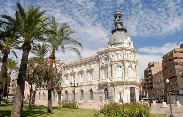 Exterior del edificio rodeado de palmeras y jardines bajo cielo azul