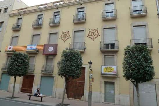 Fachada exterior del Centre d'Amics de Reus con banderas y árboles