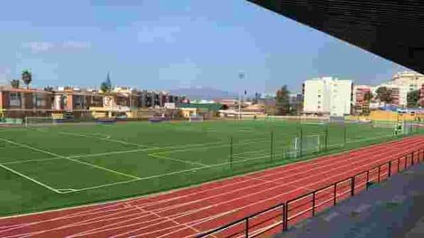 Vista panorámica del campo de fútbol Suel con pista de atletencia roja y edificios al fondo