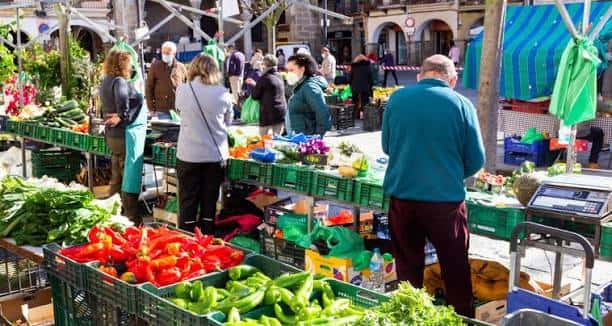 Puestos de venta de frutas y verduras frescas con clientes comprando