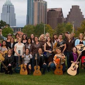 Grupo de mujeres con guitarras posando al aire libre con el skyline de Austin al fondo