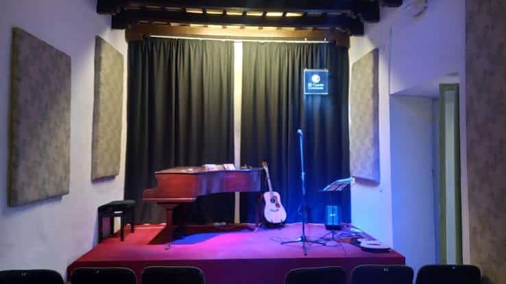 Escenario del local con piano de cola y guitarra acústica bajo iluminación tenue