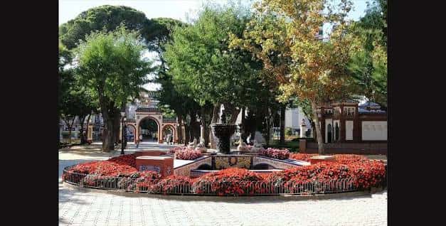 Vista general de la Fuente de las Ranas rodeada de flores rojas y árboles