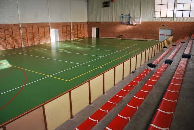 Gimnasio cubierto con cancha verde y gradas rojas