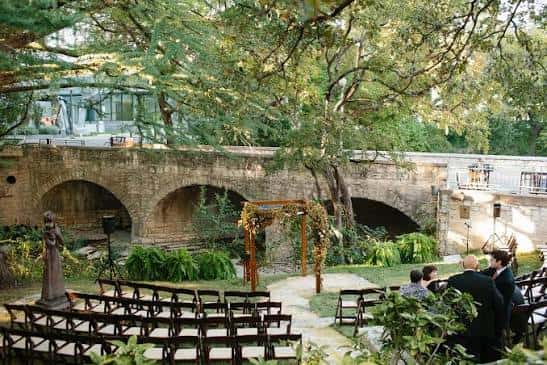 Ceremonia al aire libre en el jardín con arco floral y puente de piedra