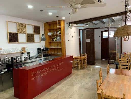 Interior del café-bar de Ca Revolta con barra roja, mesas de madera y ambiente acogedor