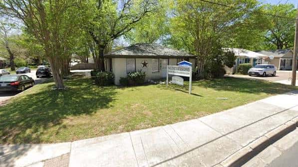 Vista exterior de la Academia de Música de Austin en un entorno residencial con árboles y césped