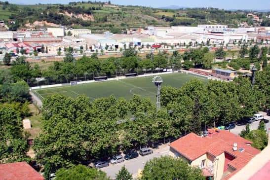 Vista aérea del Camp Municipal de Futbol Primer de Maig rodeado de árboles y edificios urbanos