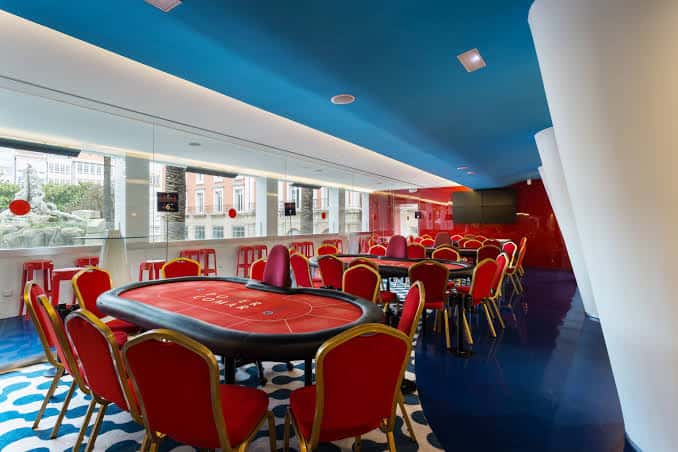 Sala de juegos interior con mesas de ruleta y sillas rojas bajo techo azul