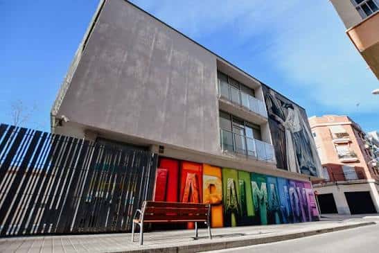 Exterior del centro cultural bajo cielo azul con banco frente al mural