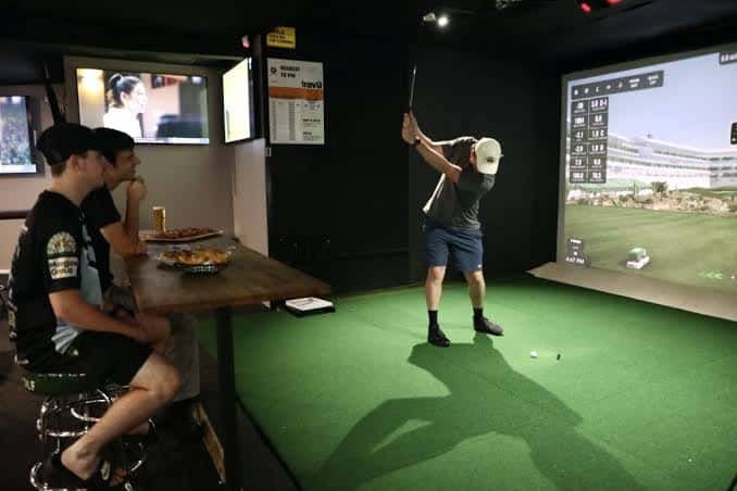 Interior del simulador de golf con clientes disfrutando y practicando swing
