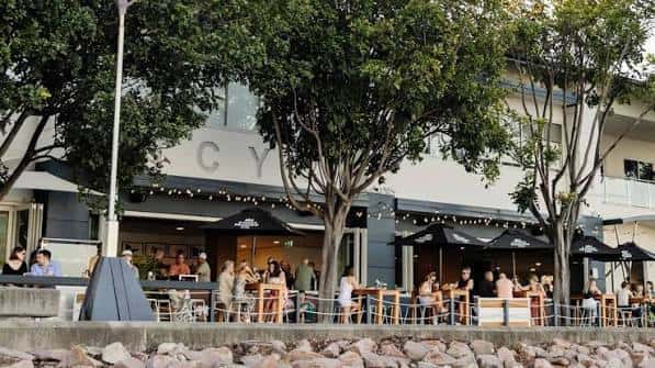 Terraza exterior del club con mesas y sombrillas junto al muelle