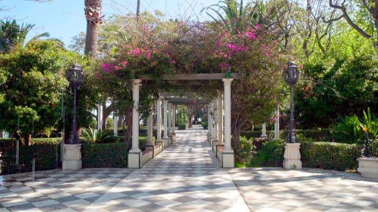 Paseo ajardinado con pérgola cubierta de flores y columnas blancas