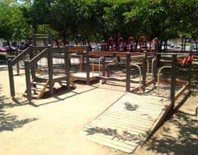 Área de juegos inclusiva con rampas de madera y estructuras accesibles bajo la sombra de los árboles