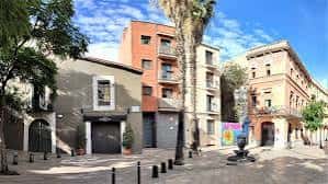 Plaza y calle de Santes Creus con edificios históricos y palmeras bajo cielo azul
