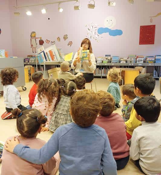 Actividad infantil en el interior de la biblioteca con lectura en grupo