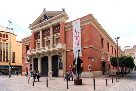 Fachada principal del teatro durante el día con cartel promocional y gente caminando