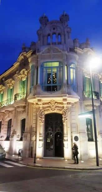 Fachada iluminada por la noche mostrando la entrada principal y ventanas decoradas