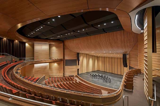Interior del auditorio con butacas rojas y techo de madera curvado