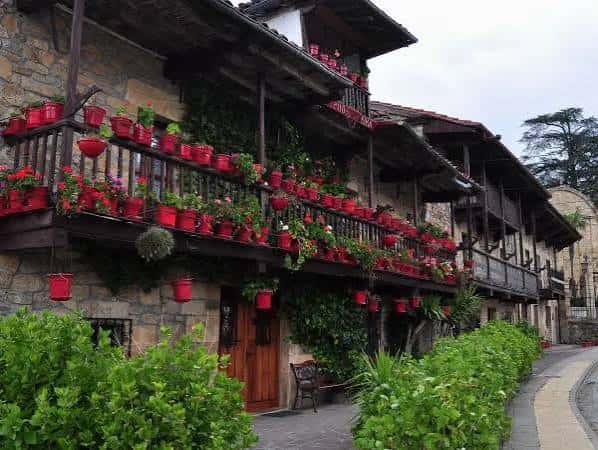 Fachada tradicional de piedra con balcones llenos de macetas rojas en el Barrio de San Ramón
