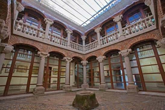 Patio interior del museo con columnas de piedra y balcón superior bajo techo de cristal