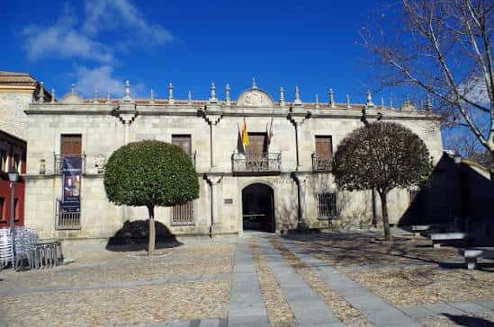 Fachada principal del Museo de Ávila con cielo azul y árboles podados