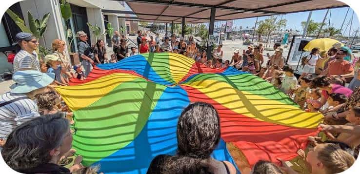 Grupo de niños y adultos participando en una actividad con un paracaídas multicolor