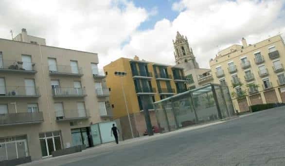 Vista general de la Plaça del Baluard con edificios residenciales y la torre de la iglesia al fondo