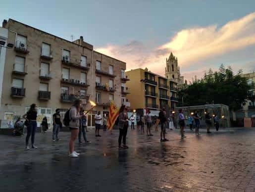 Celebración nocturna en la plaza con personas reunidas y banderas catalanas durante el atardecer