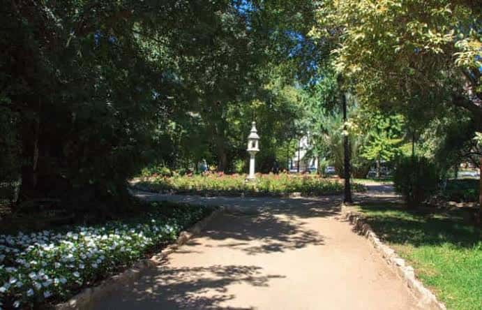 Sendero arbolado en el interior del parque con flores blancas y farola decorativa