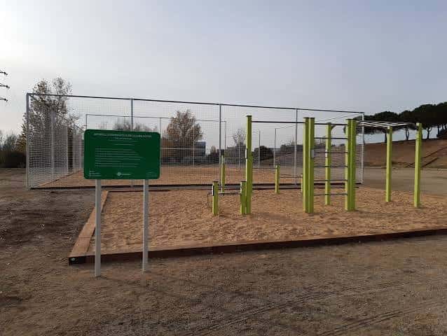 Zona de ejercicio con barras verdes y panel informativo en el parque