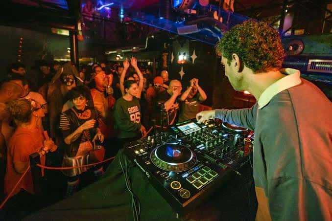 DJ actuando en Mecha House Club con público animado y luces de neón