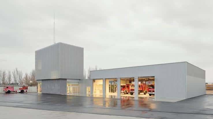 Edificio industrial contemporáneo con estructura metálica y puertas abiertas mostrando vehículos rojos